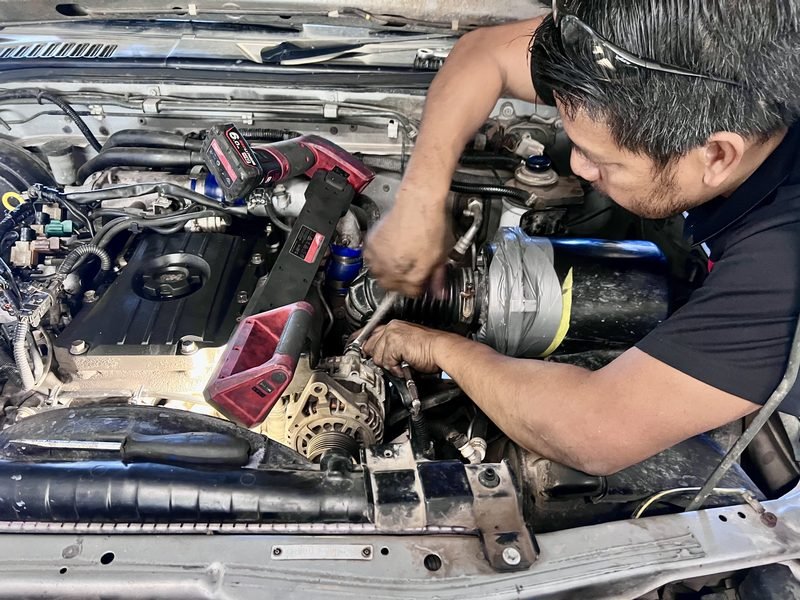 Mechanic reaching into an engine bay to work on the front of the engine with a socket