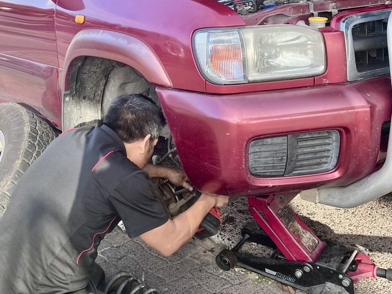 Mechanic working on the front wheel and brake of a four wheel drive raised on a jack, coil spring on the ground
